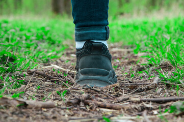 sneakers on the path. girl stands with her foot in the woods. illustration of travel. black shoes on a natural background. hiking concept