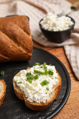 Bread with cottage cheese and green onion on wooden table, closeup