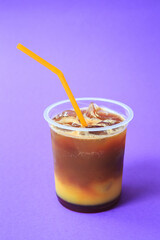 A glass with orange coffee cocktail cold refreshing drink or beverage with ice on violet background