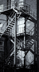 Obraz premium Linear shadows cast by sunlight on exterior metal fire escape of old building. Street in Dublin, Ireland. Deliberate grainy texture effect in monochrome black and white