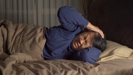 Unhappy elderly old Asian woman, person is terrified from disturbing nightmare, sleeping with stress on bed in bedroom at home. Insomnia.