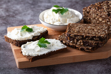 Rye bread on a wooden cutting board with curd cheese and ricotta and herbs. Decorated with green herbs