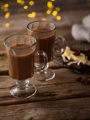 Romantic composition - two glass cups of cocoa, chocolate, sweets. Lights flicker in the background. Wooden texture. Christmas, New Year, a cozy family dinner. Close-up.