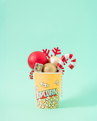 Christmas creative concept of New Year red decoration in popcorn box. Winter snack for the cinema on pastel mint background.