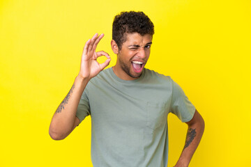 Young handsome Brazilian man isolated on yellow background showing ok sign with fingers