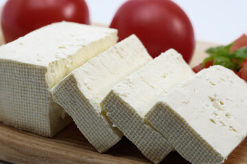 Close up feta cheese slices, ripe tomatoes, basil on a wooden board