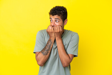 Young handsome Brazilian man isolated on yellow background nervous and scared putting hands to mouth