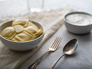 Serving ravioli, sour cream sauce, spoon and fork on a white plate. Served table for one person. White background, pastel colors. Menu design, culinary blog, instagram.