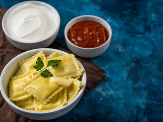 Italian ravioli drizzled with melted butter, garnished with a green mint leaf and two sour cream and tomato sauces. Dark blue background. Restaurant, hotel, cafe, home cooking.