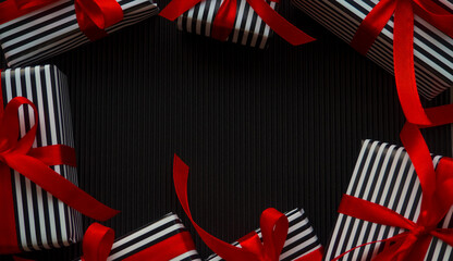 Gifts on the black background. Small gifts in a stripped black and white wrapper and with red ribbons on the dark corrugated cardboard. Christmas sale shopping. Black Friday and Cyber Monday.