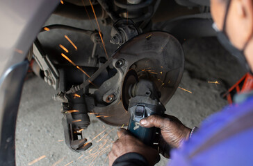 Fototapeta na wymiar A mechanic's hand uses a grinding tool to repair the steel parts of the car's drive wheels.