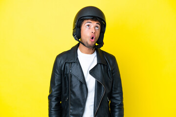 Young Brazilian man with a motorcycle helmet isolated on yellow background looking up and with surprised expression