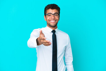 Young business Brazilian man isolated on blue background shaking hands for closing a good deal