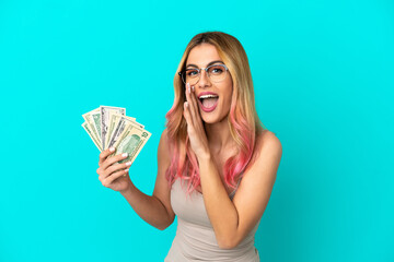 Young woman taking a lot of money over isolated blue background whispering something