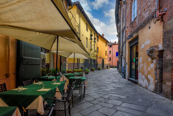 Fototapeta na wymiar Narrow old cozy street with tables of restaurant in Lucca, Italy. Lucca is a city and comune in Tuscany. It is the capital of the Province of Lucca