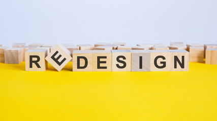 the word redesign is made of wooden cubes lying on a yellow table. one of the cubes is placed on an edge, concept