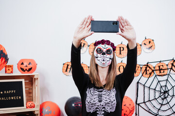 woman wearing mexican face mask during halloween celebration. taking selfie with mobile phone....