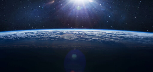 Wide wallpaper of Earth surface in outer space. Orbit of planet. Sun light and stars on background....