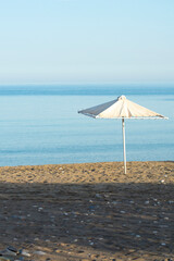 Lone parasol on a sandy beach at  secluded Sikinos island, Greece. Vertical shot with copy space.
