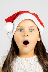 close-up portrait of surprised, shocked, open-mouthed girl in red Santa Claus hat, isolated on white background with copy space. 