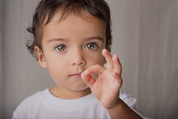 portrait of little boy with expressive eyes making sign
