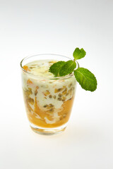 glass of healthy tropical fruit shake with mango, passion fruitc coconut milk and chia seeds decorated with mint isolated at white background.