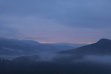 Naklejka na ściany i meble Beautiful view of mountains covered with fog during sunrise