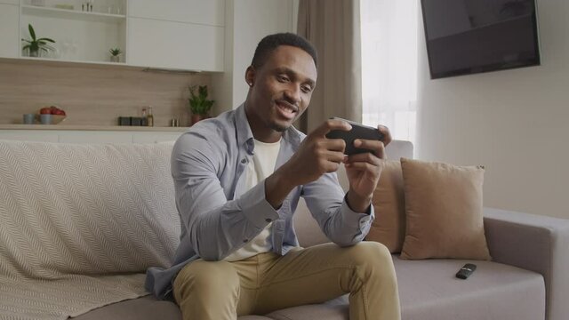 Happy smiling african american man playing on his smart phone in his apartment