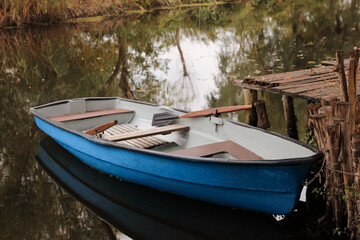 Light blue wooden boat with oars on lake near pier