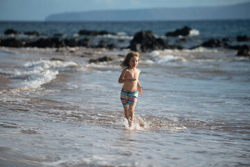 Happy boy running beach near the seaside. Excited amazed kid having fun with running through water in ocean or sea.
