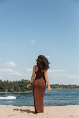 Naklejka premium A young sexy woman barefoot and in a summer dress walks along the edge of the river