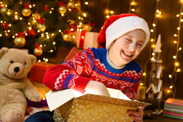 Child girl posing in new year or christmas decoration, wearing a red sweater and a Santa hat, she opening a gift box and having fun. Holiday lights and lots of gifts, Christmas tree with toys.