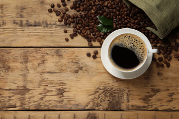 Cup of aromatic hot coffee and beans on wooden table, flat lay. Space for text