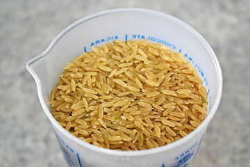 Brown rice grains on measuring cup in the kitchen