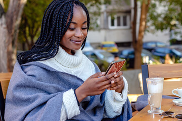 Beautiful young black girl relaxing in a coffee shop chatting and texting on social networks on her...