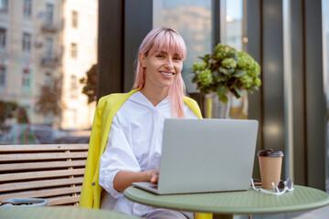 Joyful young woman using laptop at outdoor cafe