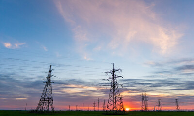 silhouette of high voltage power lines against a colorful sky at sunrise.