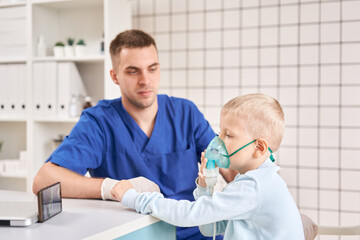 Fototapeta premium A pediatrician diagnoses lung disease and provides treatment. Breathe the medicine through a nebulizer inhaler.. Portrait of adorable little boy visiting doctor.