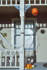 Halloween decorations of raw pumpkins, and hanging orange Jack o Lantern on sunny porch of old house - 465857466