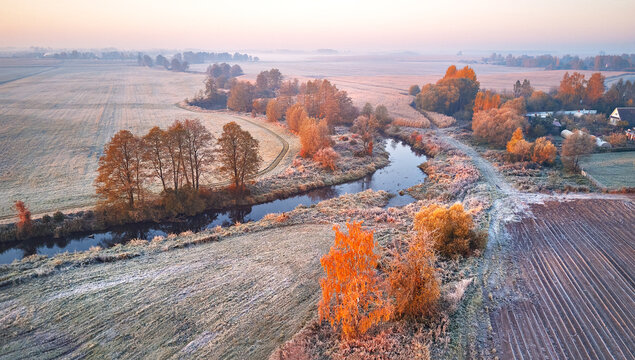 Frost on grass. River, field, meadow, village, fall color trees. Sunrise morning aerial panorama