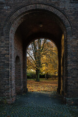 Blick durch ein Tor des Säulengangs auf die Herbstbäume im historischen Berliner "Friedhof am Columbiadamm"