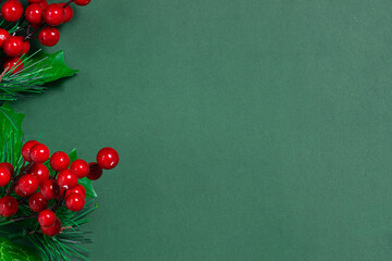 Red holly berries with leaves on trendy dark green background. Minimalism style Christmas card. Copy space for your design.