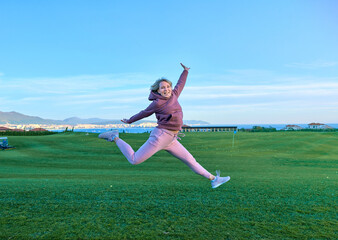 Happy girl golfer jumping in the air with raised arms and golf club in hand after successful shot.