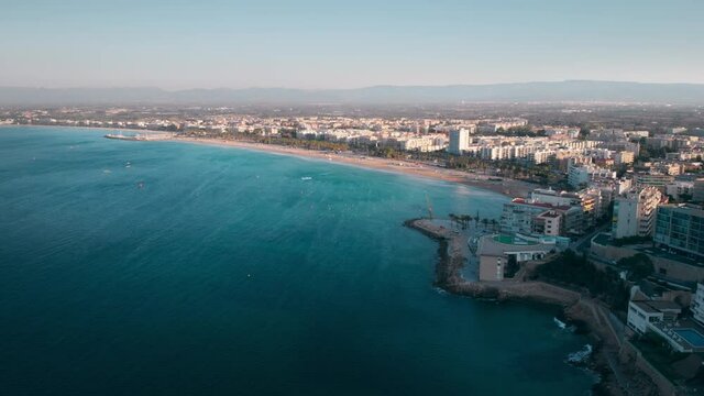 Beautiful aerial panorama of the Mediterranean coastal city of Salou in Spain. Top view from the sea with its turquoise waves to the beach, green alleys and building on the shore.