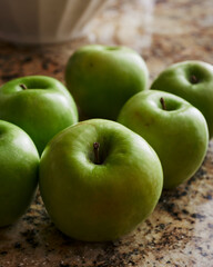 Granny Smith apples whole on granite countertop with large bowl in background.