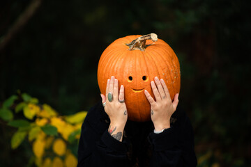 person with a pumpkin on their head hiding behind a tree with vines