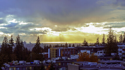 Nightfall at Univercity Highlands on Burnaby Mountain with sunlight filtering through dark rainclouds onto horizon.