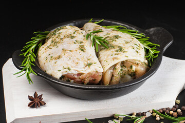Top of view.Raw chicken marinated.Raw marinated chicken thighs in a light sauce with herbs and spices on a dark background with herbs. Chicken half-cooked thighs. Copy space.