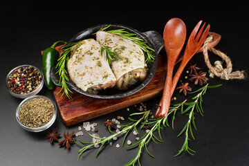 Raw chicken marinated.Raw marinated chicken thighs in a light sauce with herbs and spices on a dark background with herbs. Chicken half-cooked thighs. Top of view.