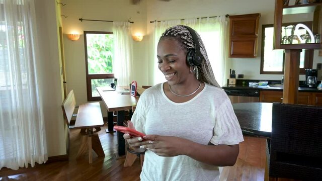 mujer afroamericana muy feliz escuchando m&uacute;sica con aud&iacute;fonos con su celular